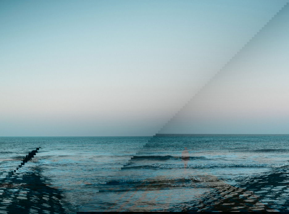 Silhouette of distant person standing on sea shore at dusk