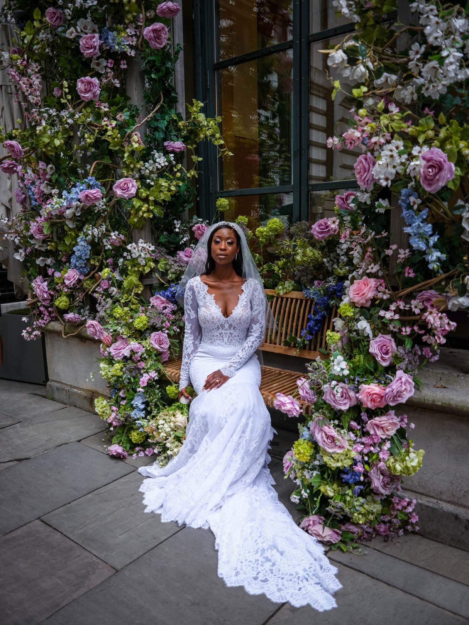 Bride sitting on a bench in front of a wall of flowers