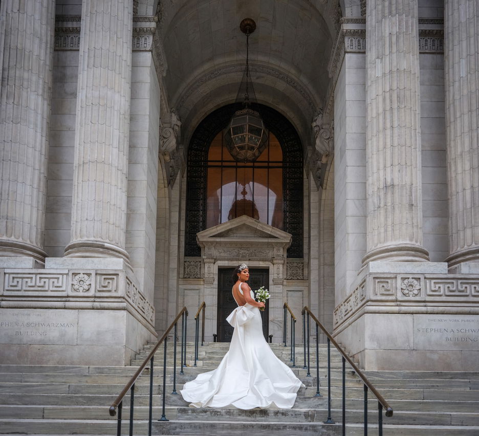 Bride in long, white dress standing on the steps of a towering, historic building