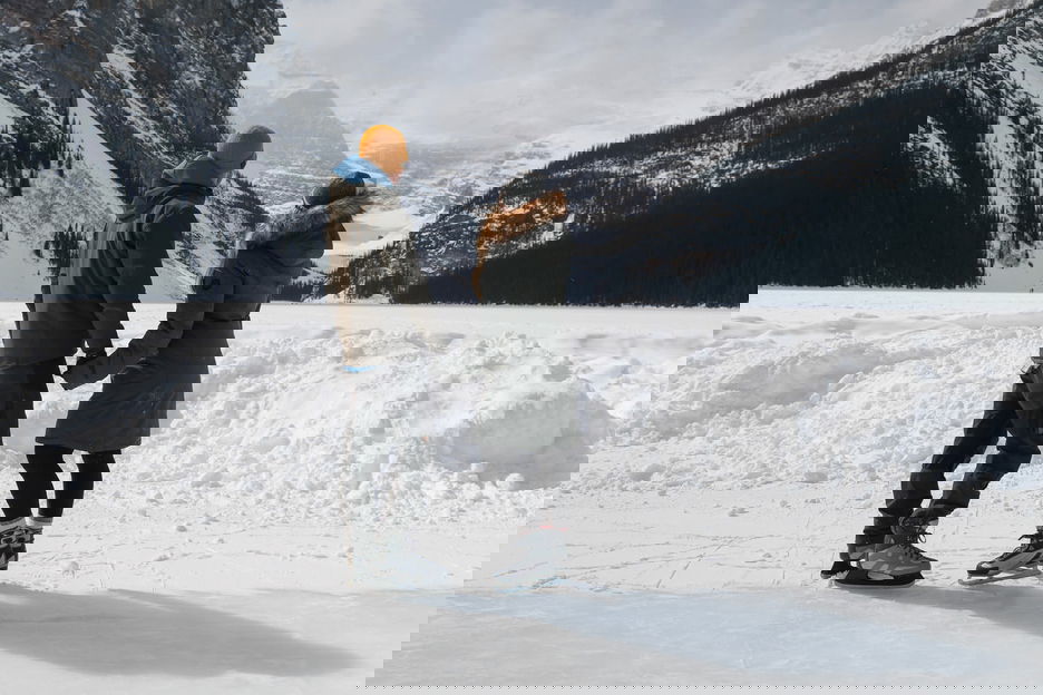 Man and woman hold hands while looking out across a snowy mountainous valley