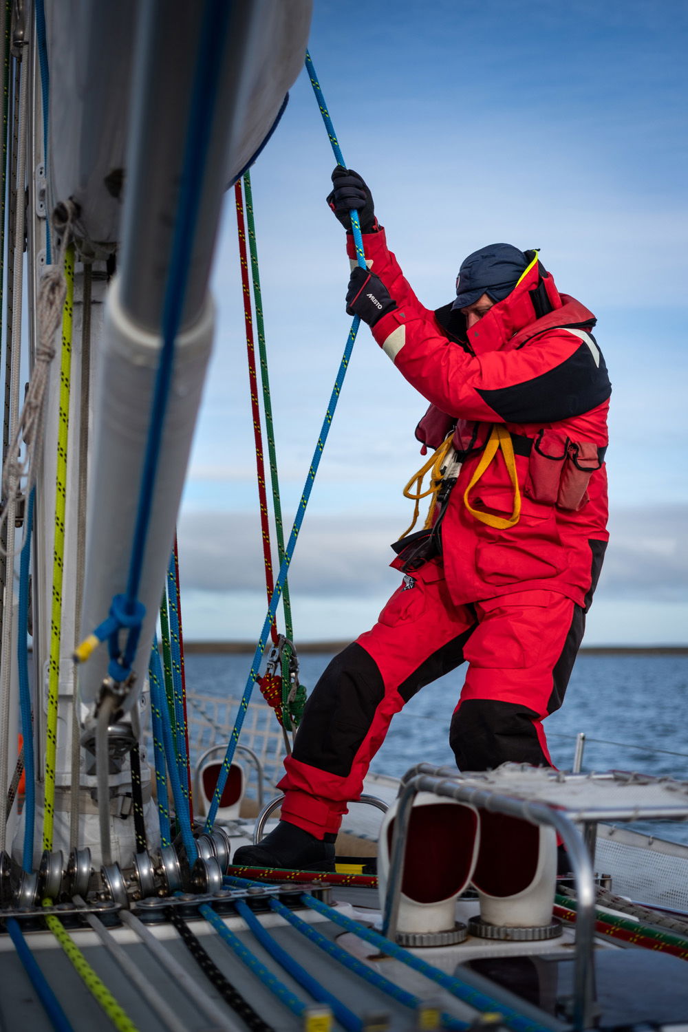 On a boat, a sailor in red waterproof gear pulls on a rope running up the mast.