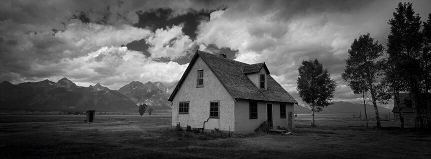 A small house surrounded by trees with mountains far behind