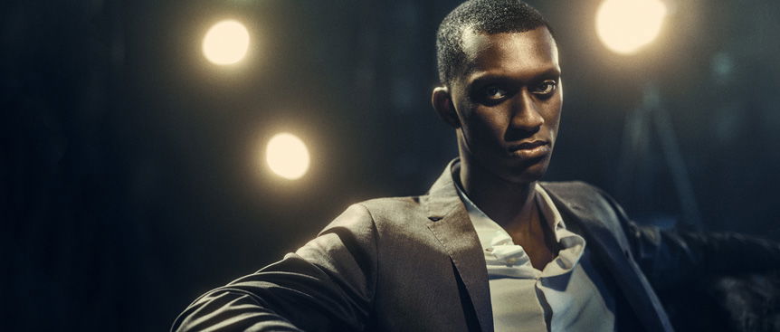 Model posing in suit jacket and shirt on a black background with individual blurred lights