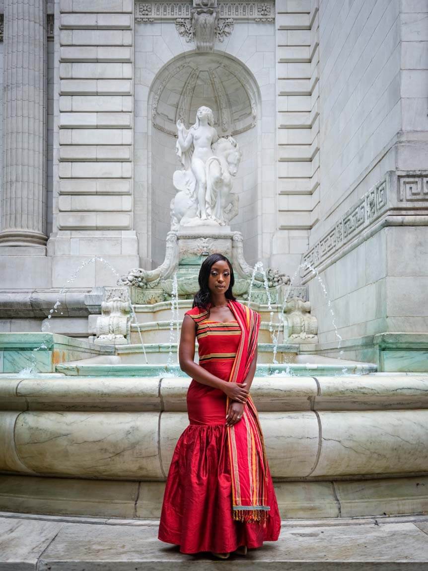Bride in red traditional African dress standing in front of fountain