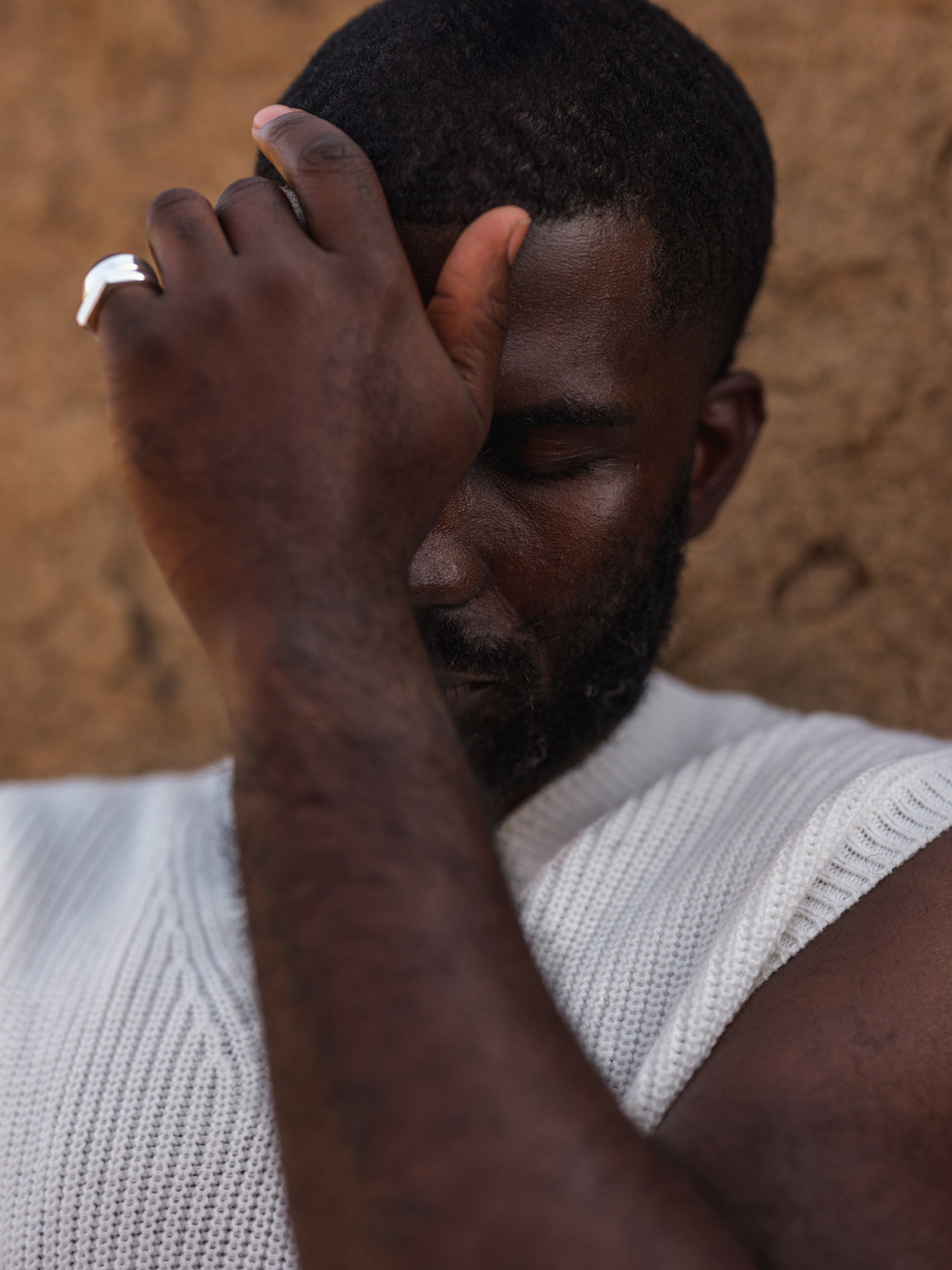 A close-up of an African-American man, holding his hand to his head, eyes closed