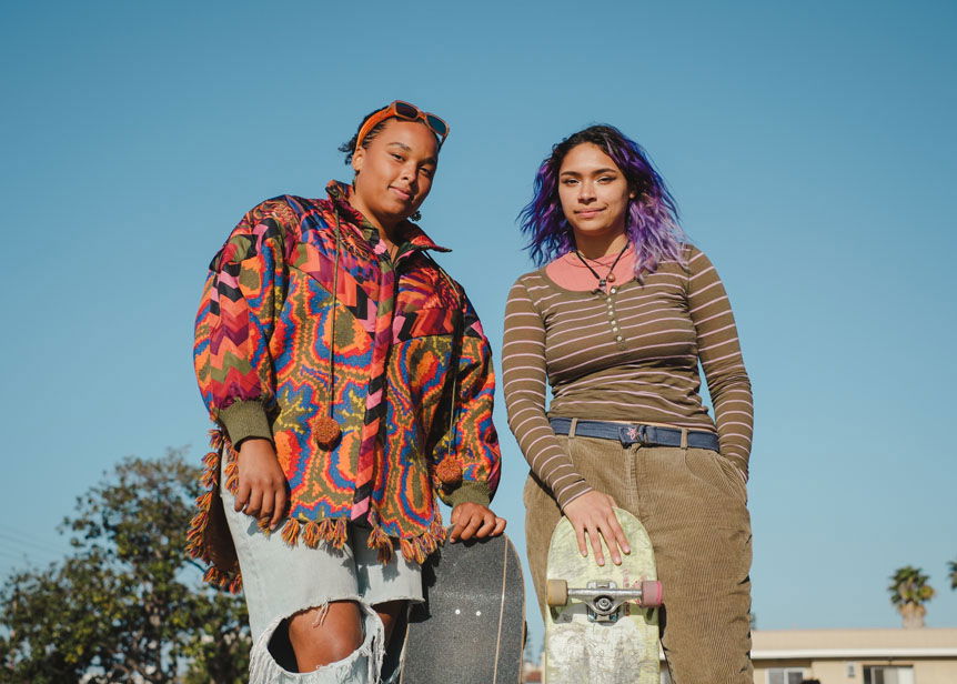 Two young women posing with their skateboards against clear blue sky