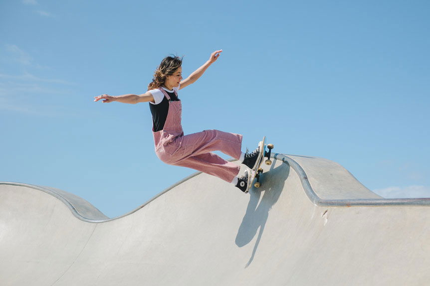 Young woman in pink jumpsuit skateboarding on California skatepark ramp