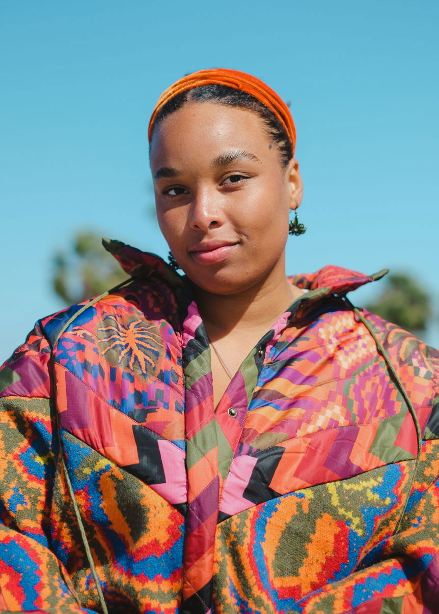 Portrait of young woman in colorful jacket, standing against clear blue sky