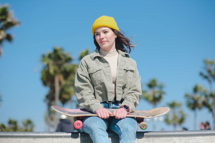Young woman in yellow hat sitting on ramp with skateboard