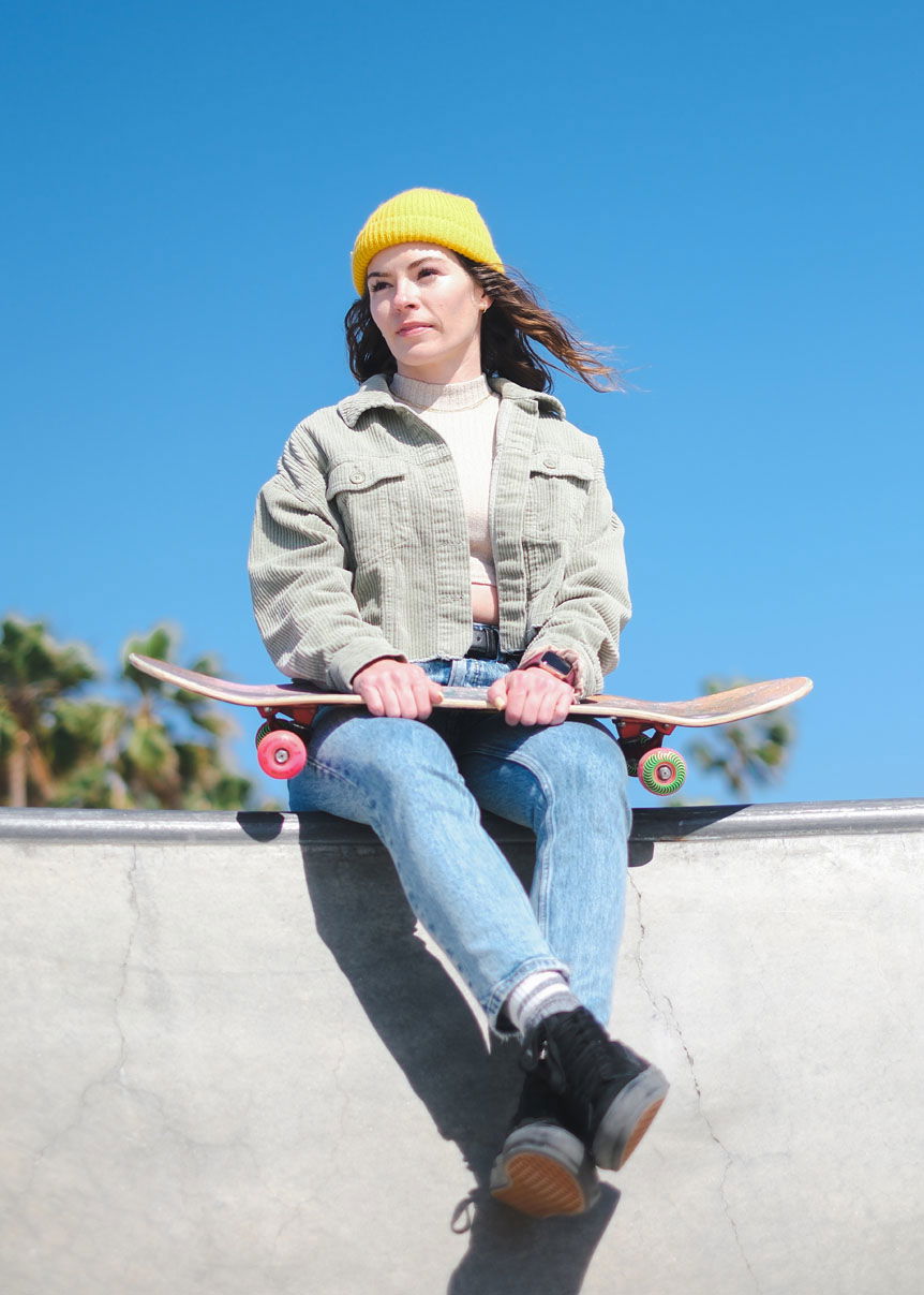 Young woman in yellow hat sitting on ramp with skateboard