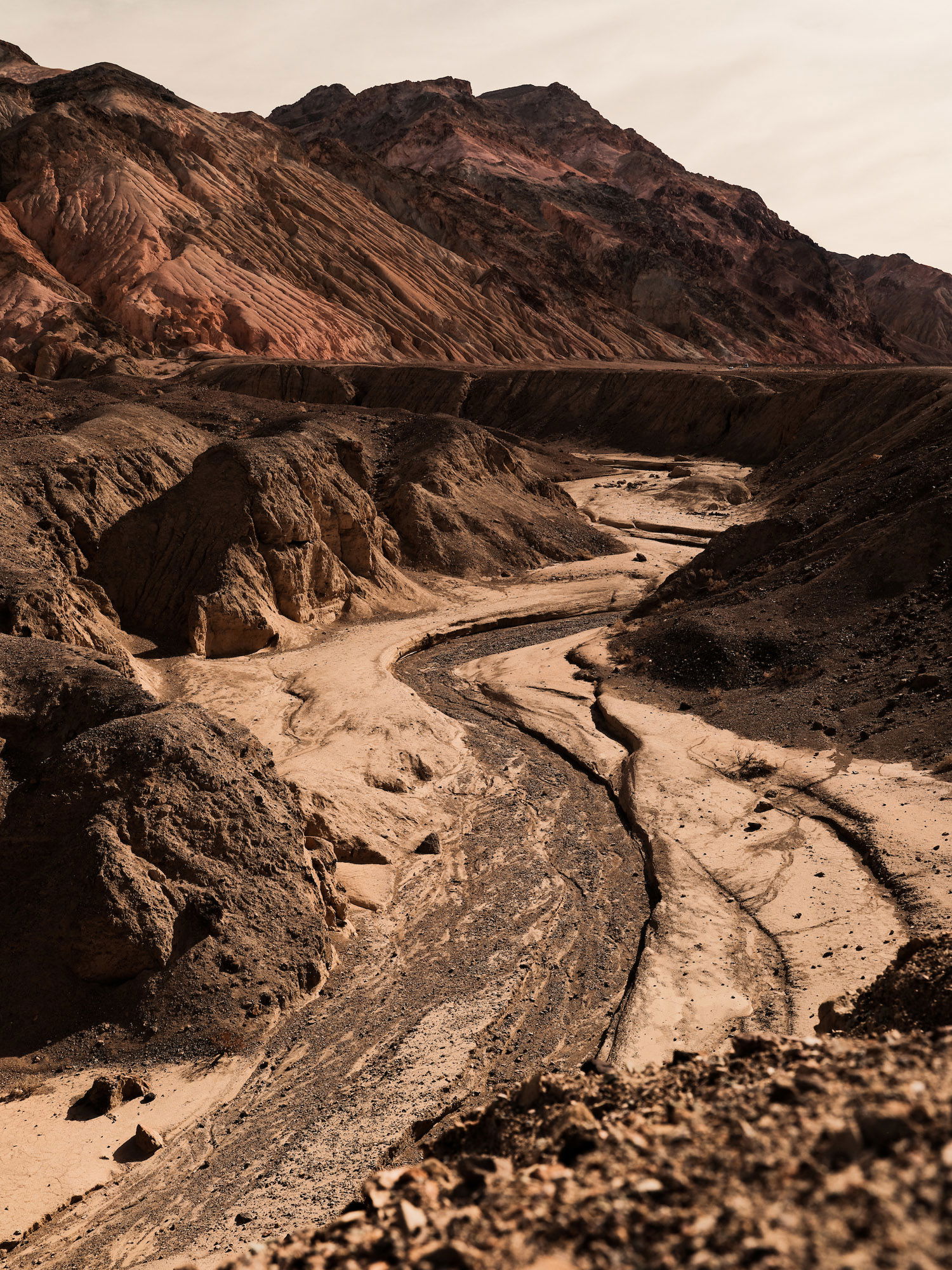 A winding pathway of sand stretches toward beige mountaintops