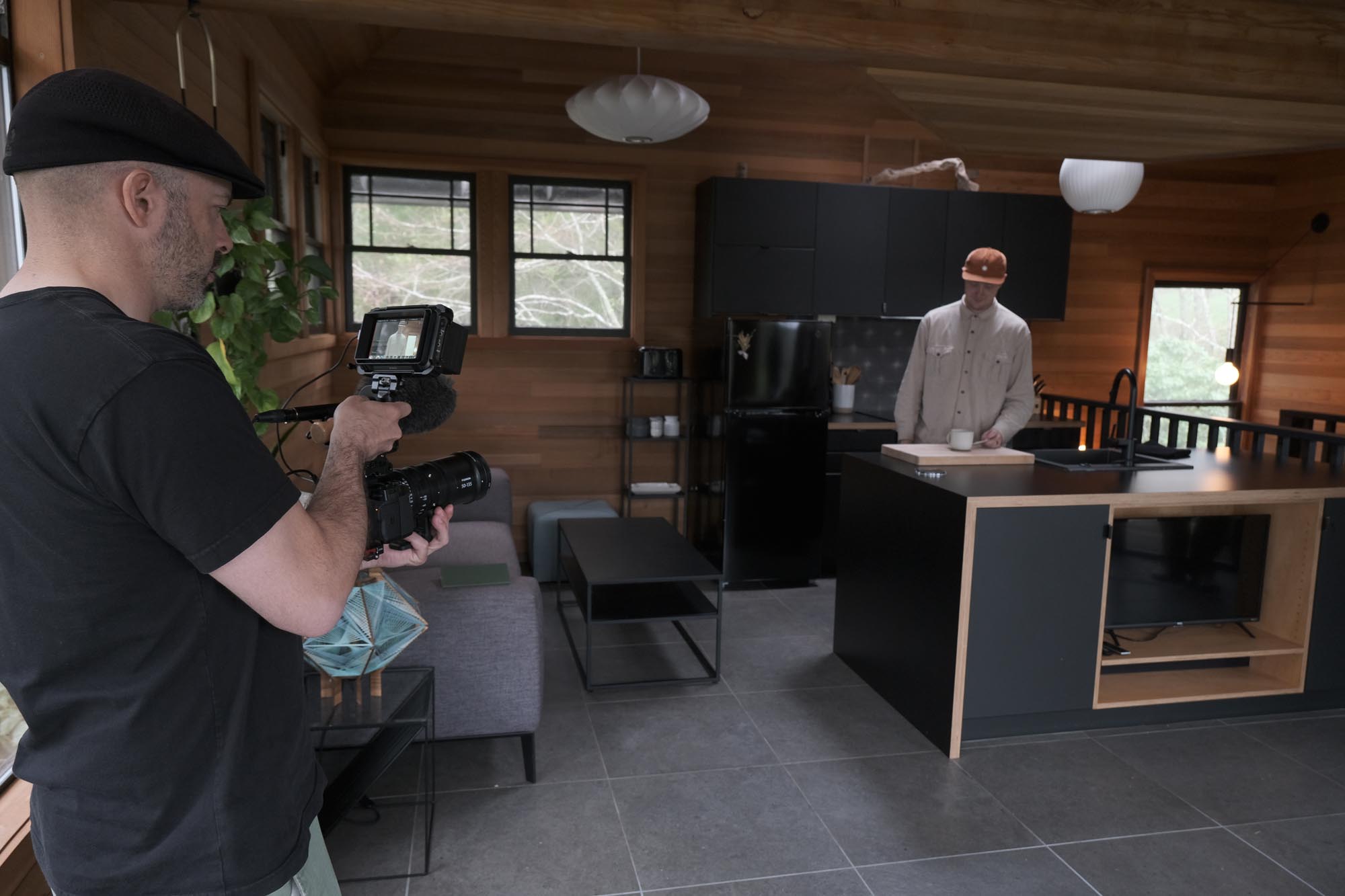 A man trains his camera on a man in a wooden kitchen