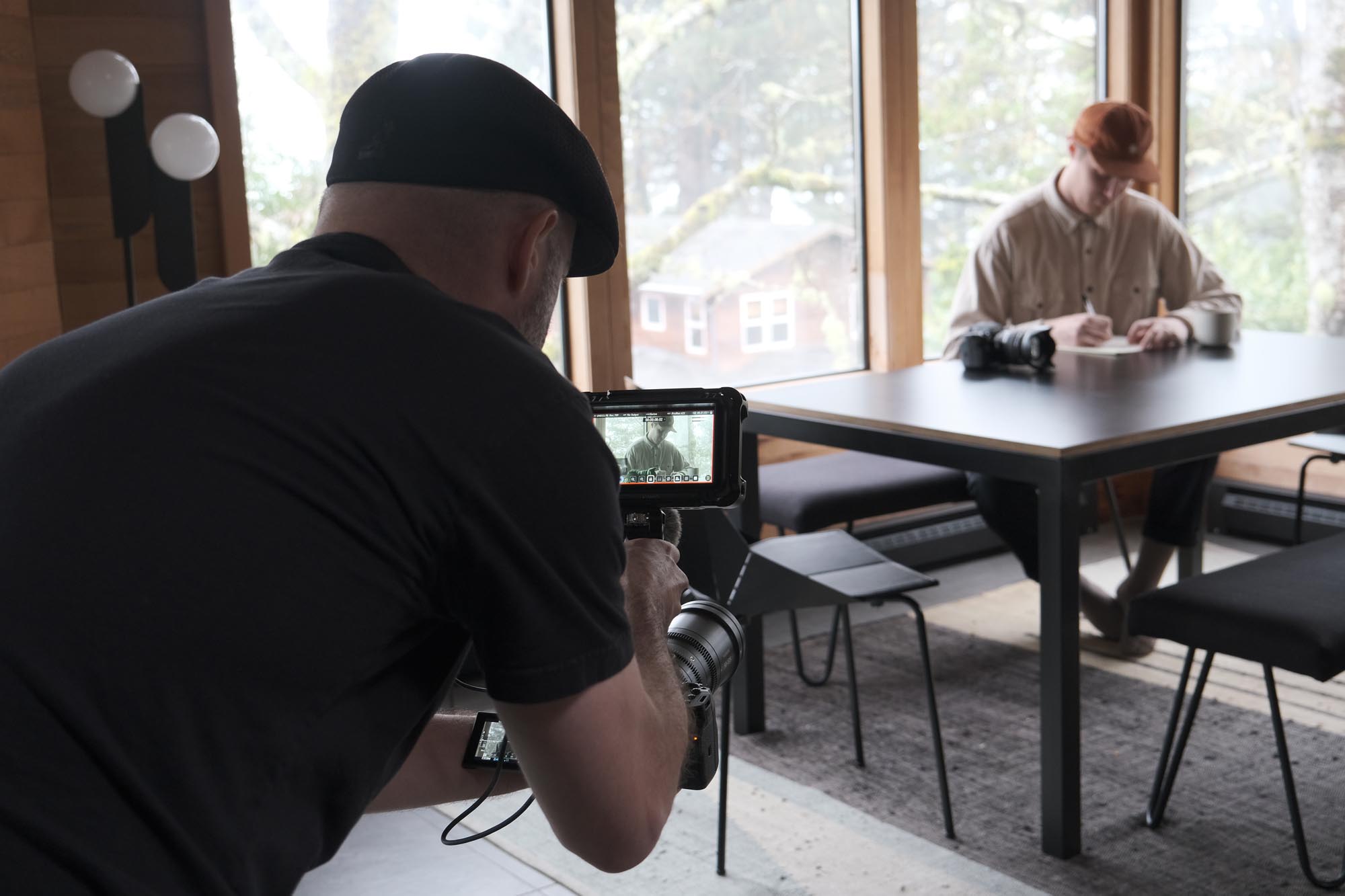 A man trains his camera on a man in a wooden kitchen