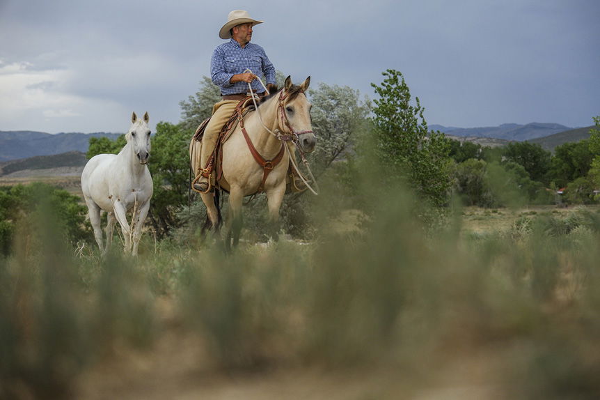 Man on horse leading second horse across plain