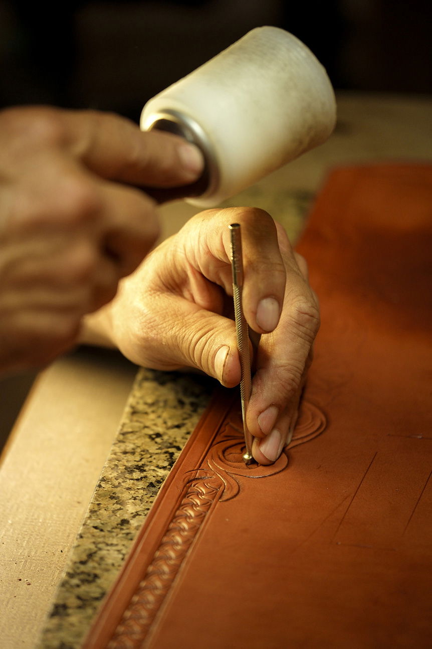 Man's hands hammering pattern into leather