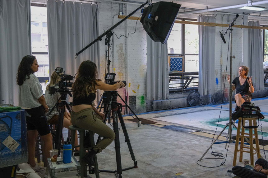 Three women filming older woman inside art studio