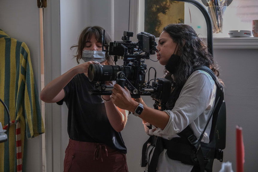 Woman holding camera on cinema steady rig while second woman consults