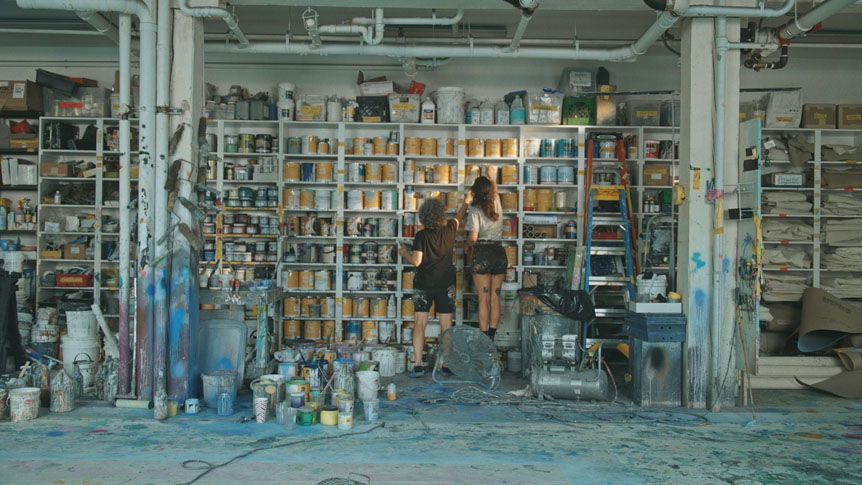 Older woman and adult daughter studying huge shelf of art supplies in studio