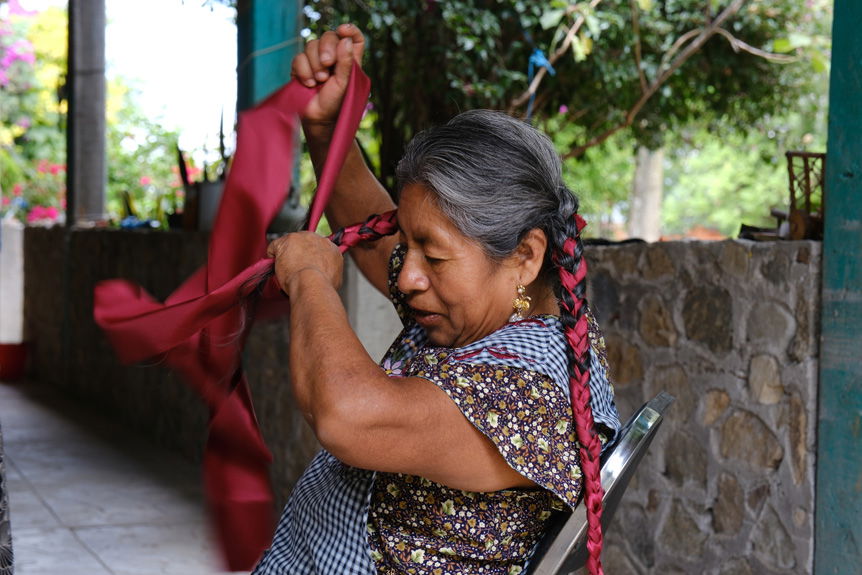 Elderly Oaxacan woman braiding hair into ribbons