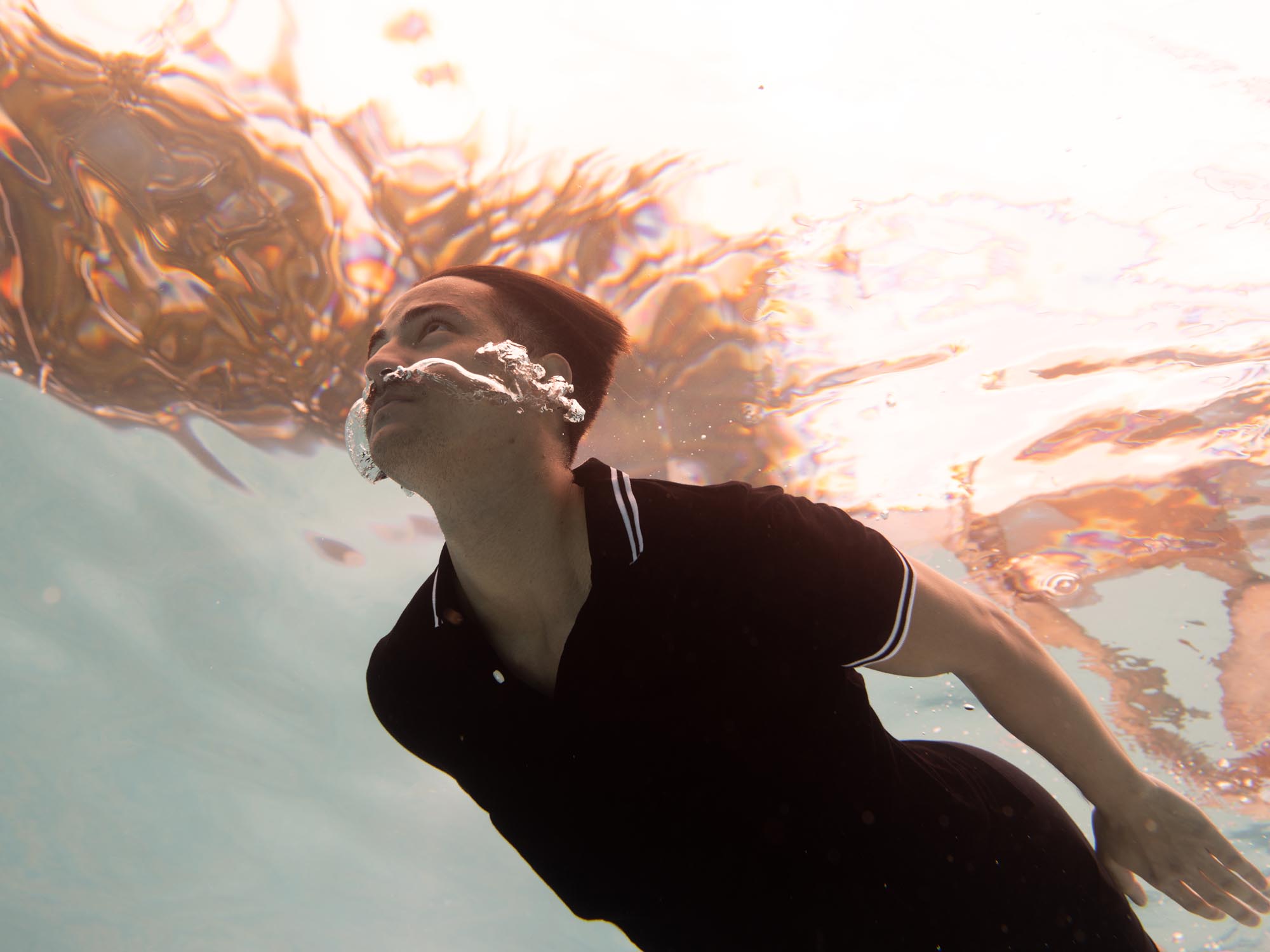 Dressed in a black polo, a man swims through the waters of a swimming pool