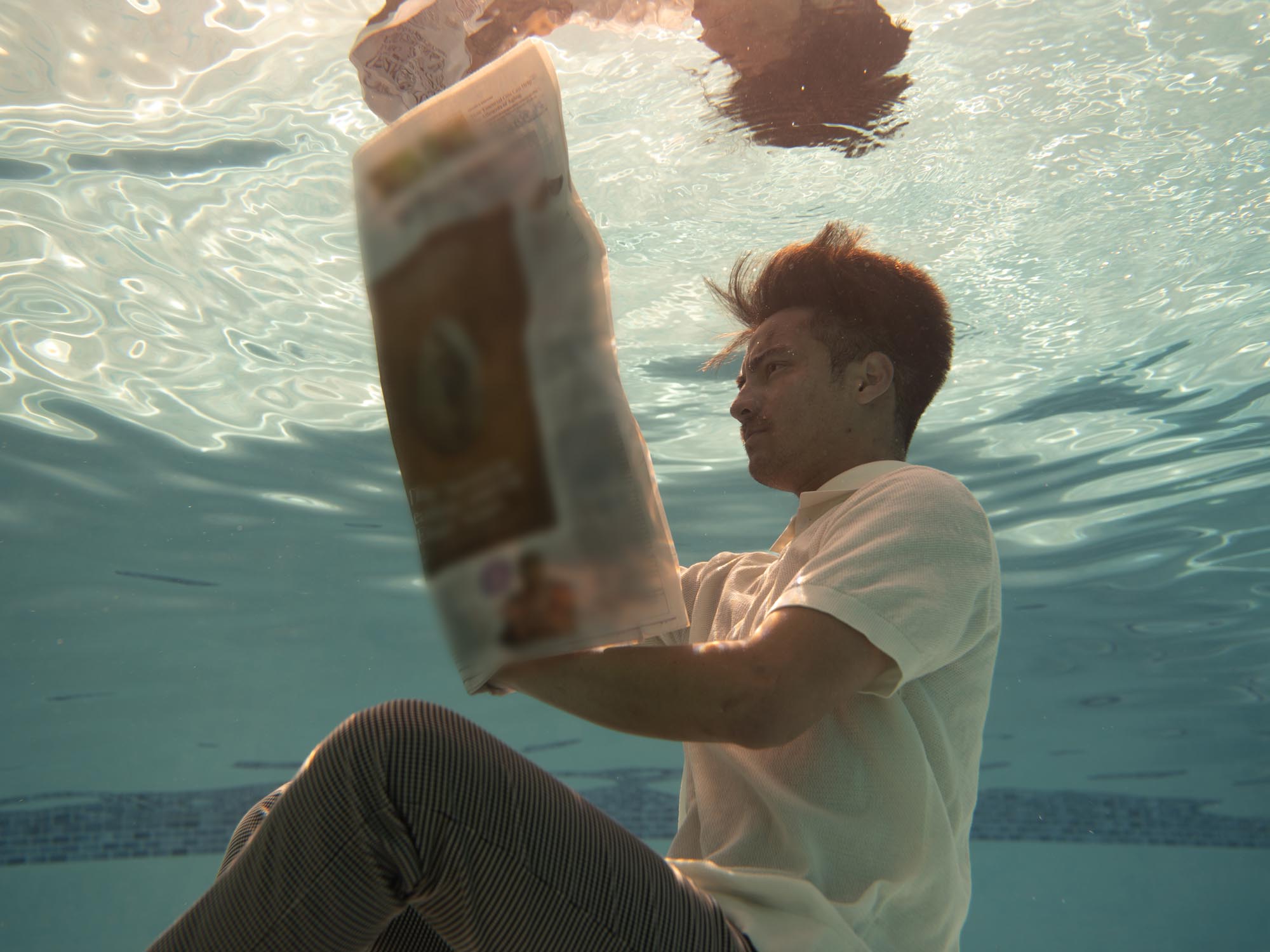 A man in a white tee studiously reads a newspaper underwater
