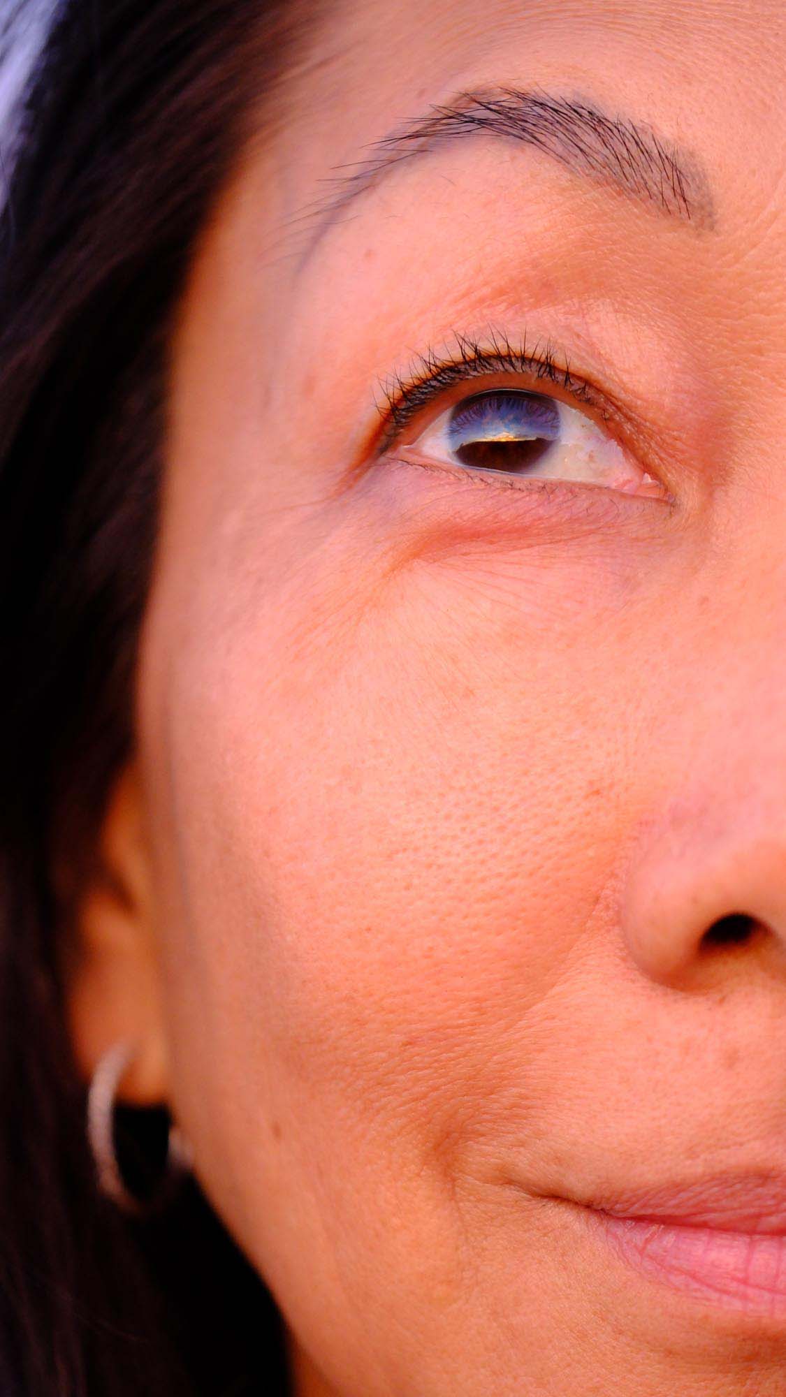 A half-face close-up of a an Asican woman, gazing intently at something above her