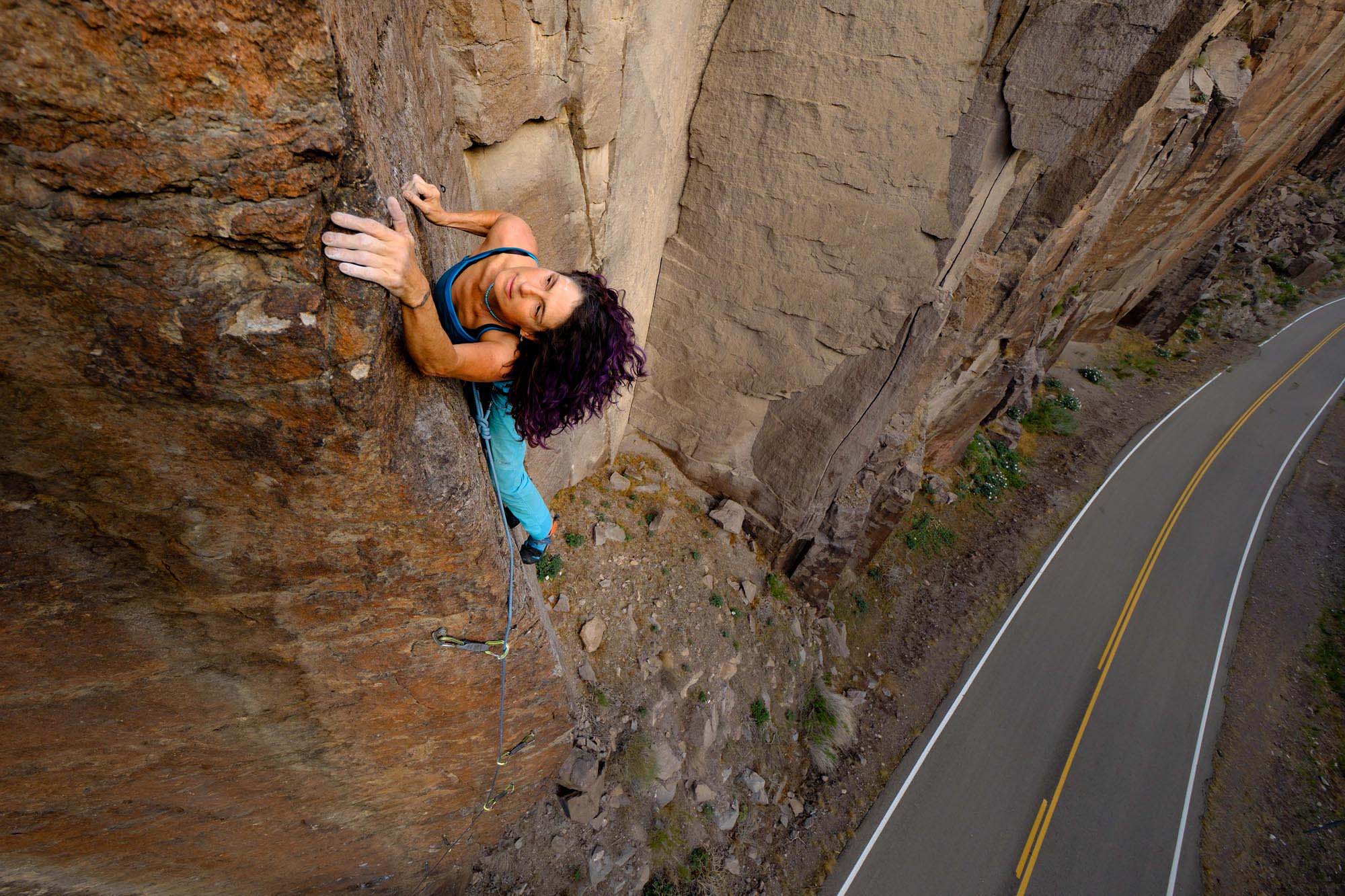 Framed against a winding highway, a woman scales a cliff face