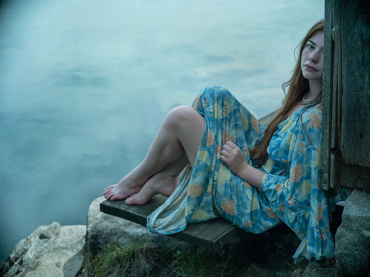 Young woman in flowing gown sitting by water