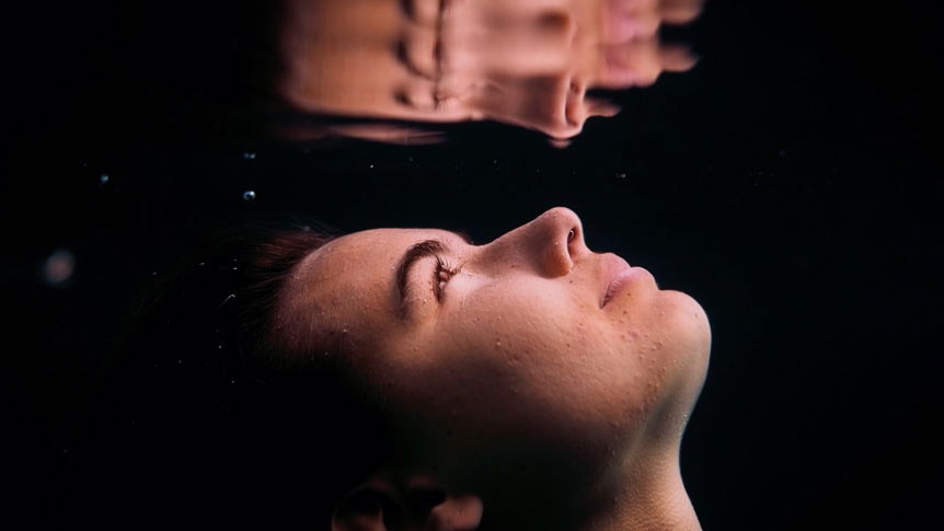 Young woman's face reflected in surface of water