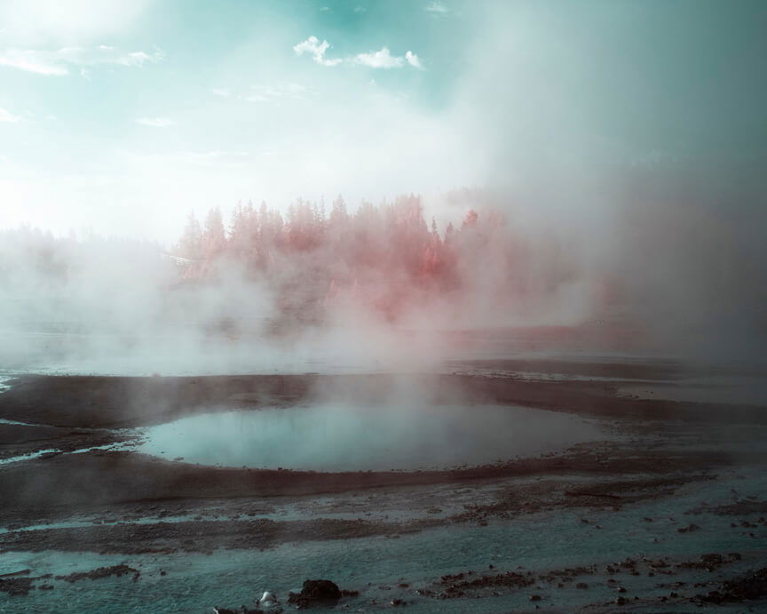 Steaming hot-spring pools with vibrant red trees on horizon