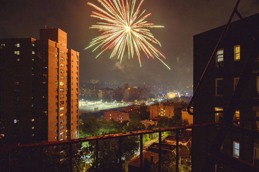 Firework exploding beyond New York city apartment blocks, seen from high-up fire escape