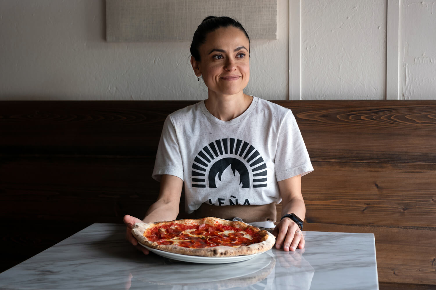 Owner of Lena restaurant sits at table with pizza on plate