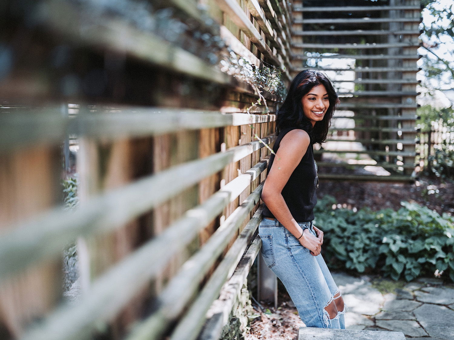 Woman wearing blue jeans and black shirt smiling leaning against wall
