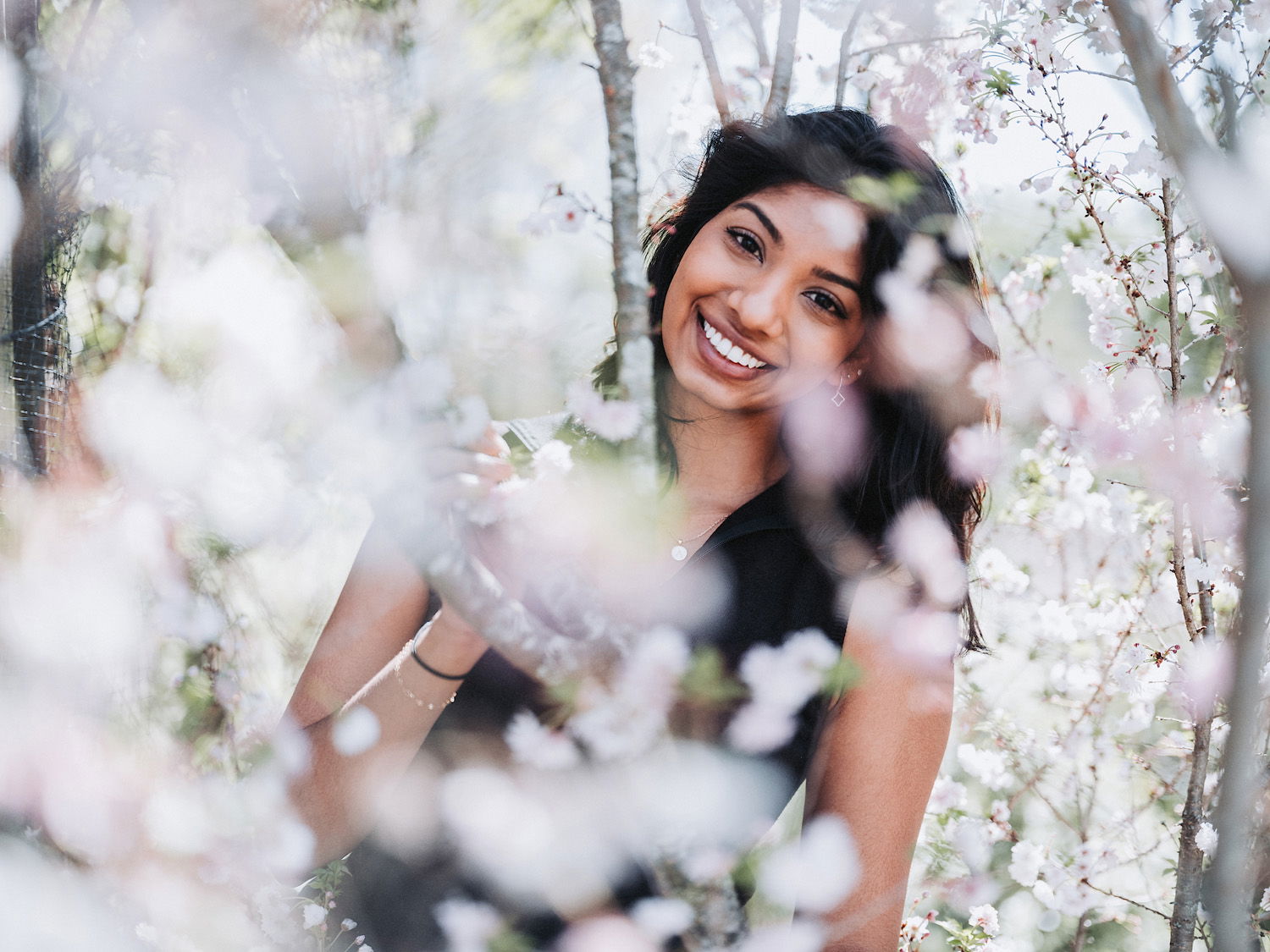 Woman with dark hair smiling for portrait among out-of-focus flowers