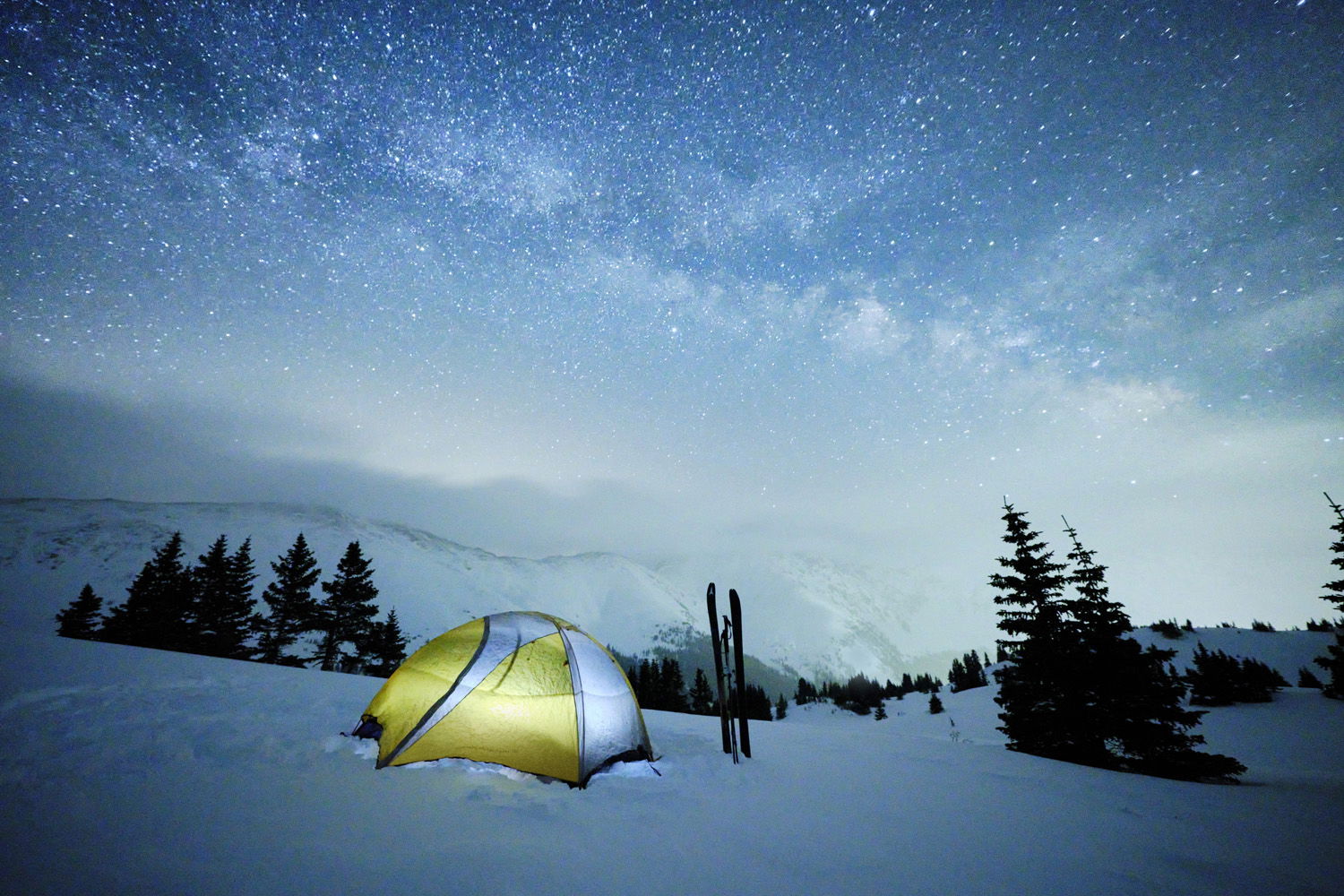 Wide shot of tent and night sky on snowy mountain