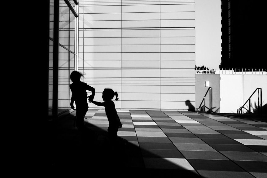 high contrast photo of two young girls playing in city square silhouetted by bright sunlight