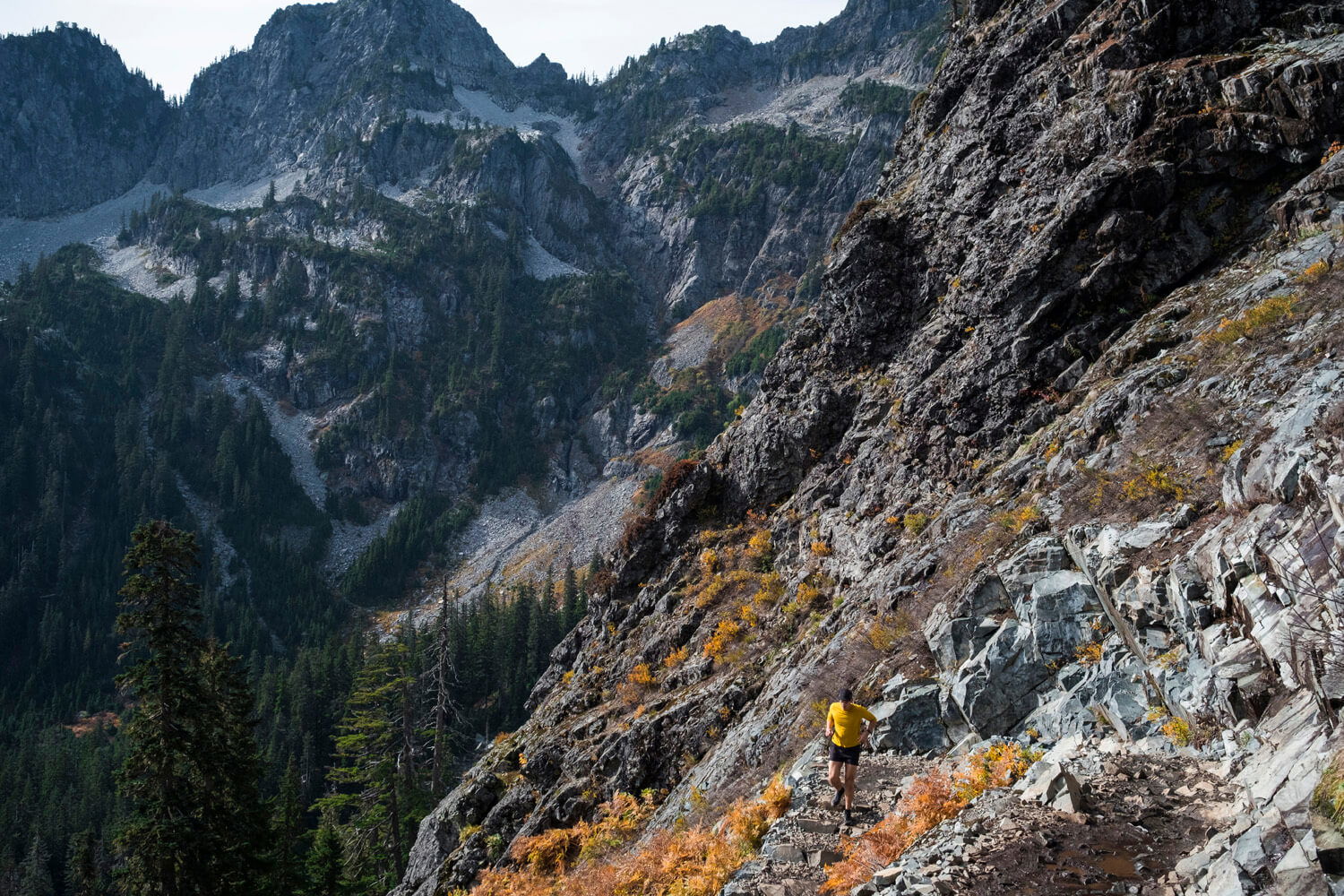 trail runner jogs along the side of a steep, rocky mountain valley