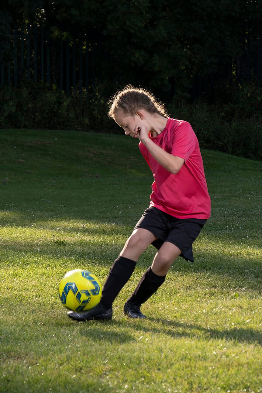 Young girl kicking football, lit with flash from one and a half metres