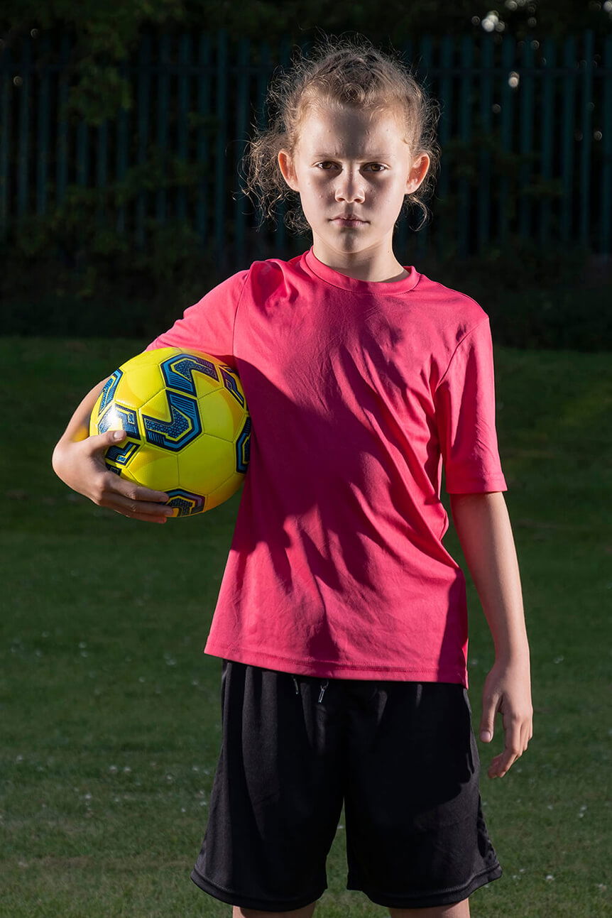 Young girl holding football, lit from both sides with flash