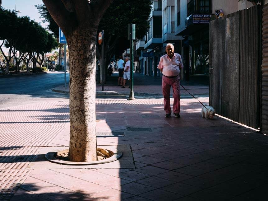 Old man walking down sunny street in the late afternoon